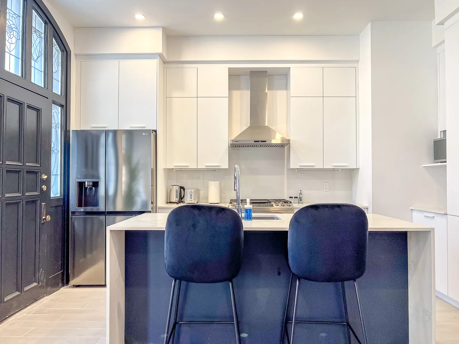 White kitchen with an island, navy bar stools and stainless appliances