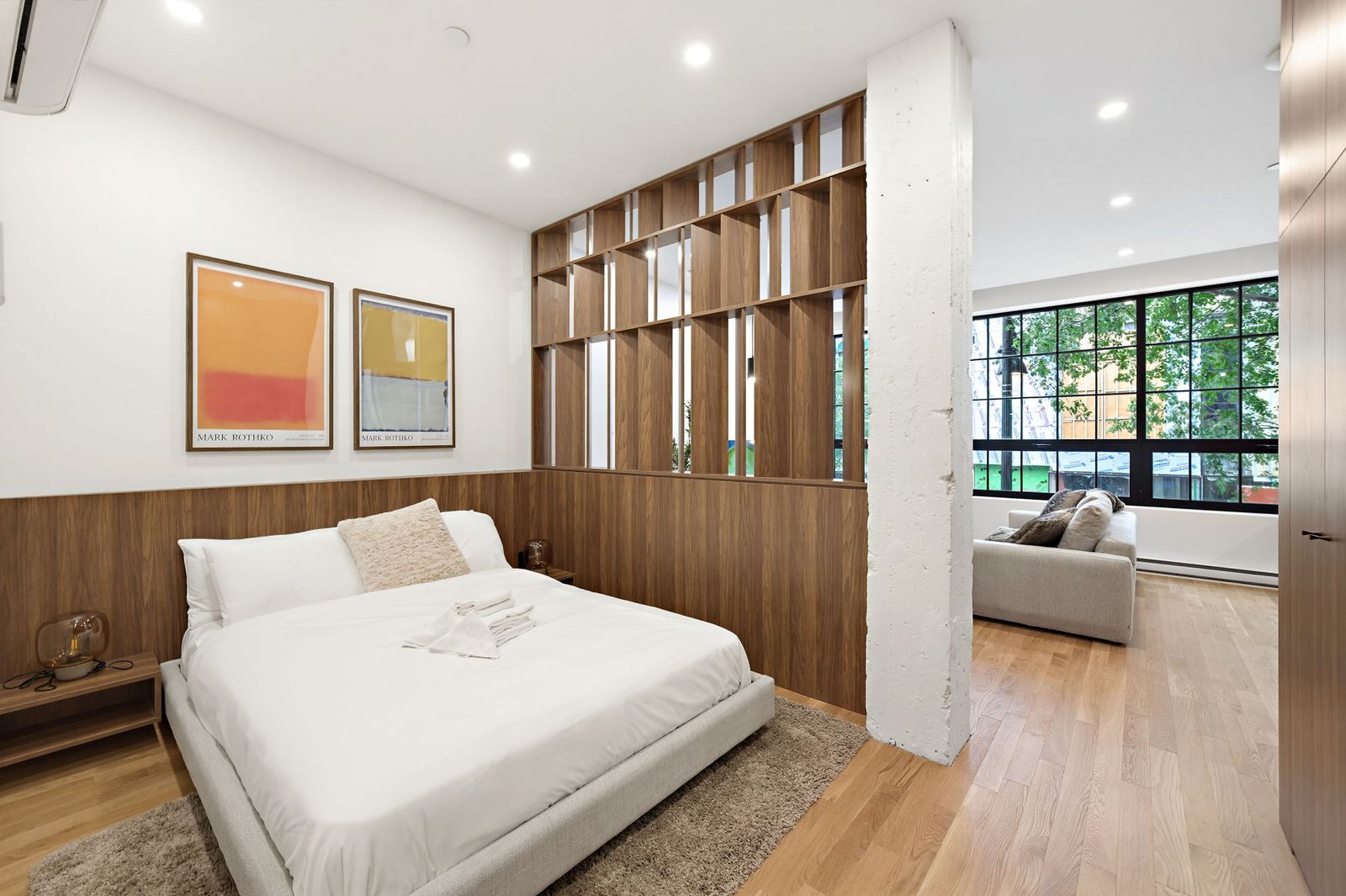 Bedroom with wood-slat divider and view into the living area